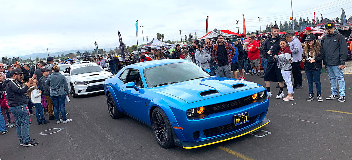 Crowd of Spring Fest attendees taking pictures of a line of cars coming into the event