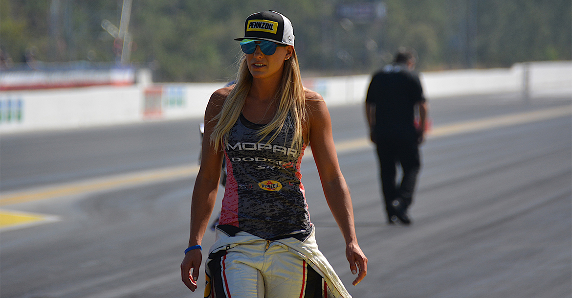 Leah walking down the track wearing a Pennzoil hat and race suit