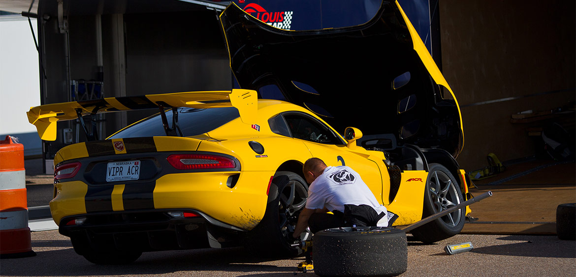 a man changing the tire on a yellow dodge viper