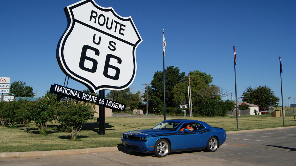 a man driving a 2009 Challenger R/T Classic in B5 Blue parked next to the route 66 sign
