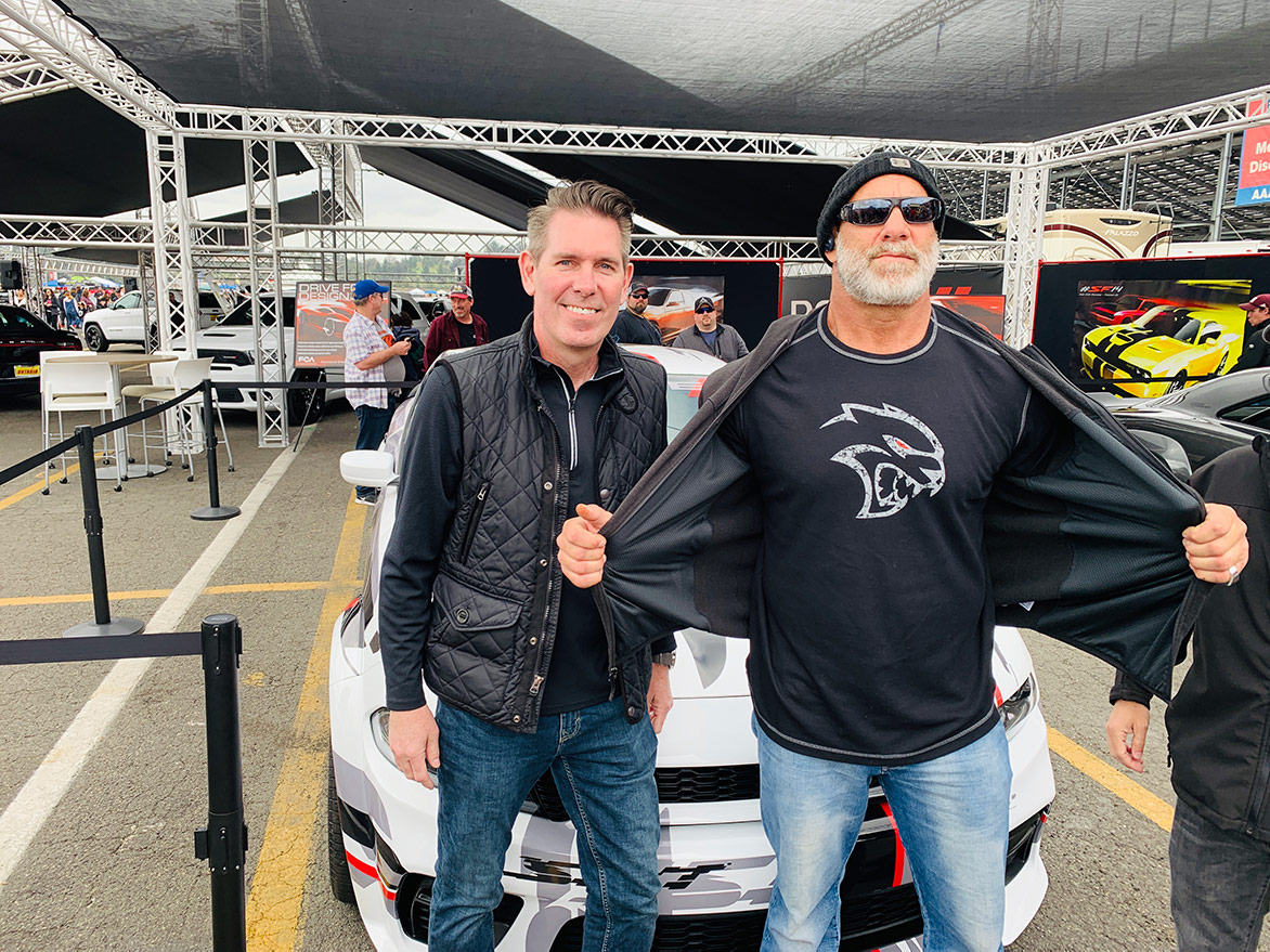 two men standing in front of a white vehicle 