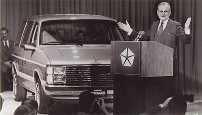 lee iococca speaking on a podium in front of a car