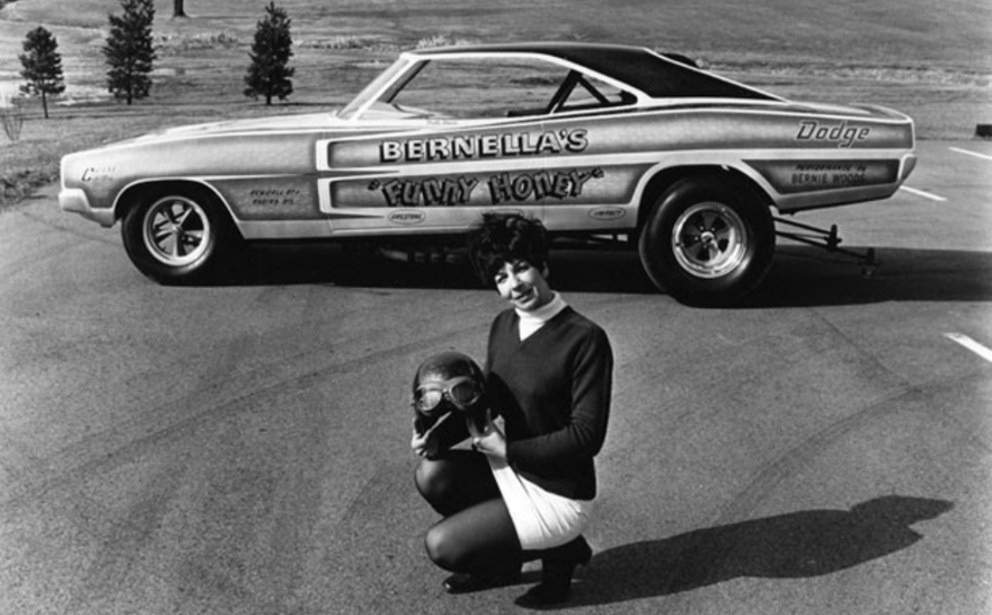 Person kneeling in front of a classic funny car