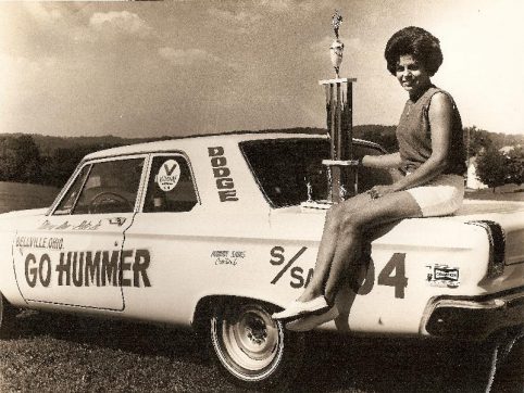 Mary Ann Foss sitting on the trunk of her race car holding a trophy