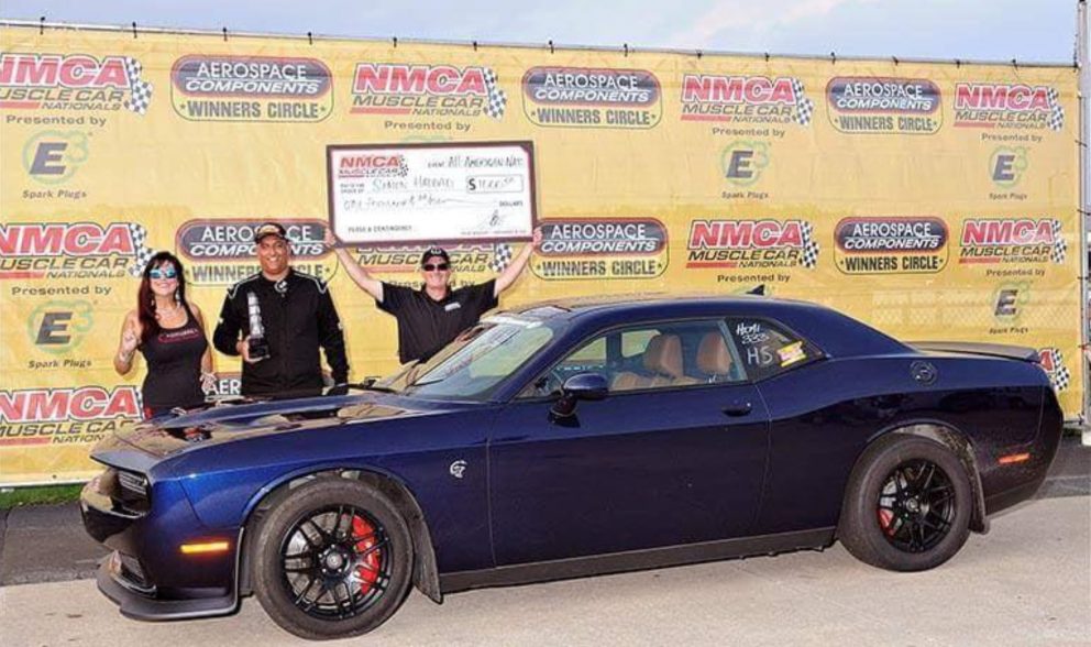 People standing behind a Dodge vehicle after winning a race