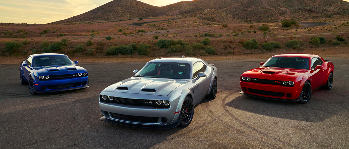 two Dodge Challenger SRT Hellcat Red eyes and one Dodge Challenger SRT Hellcat parked by some mountains