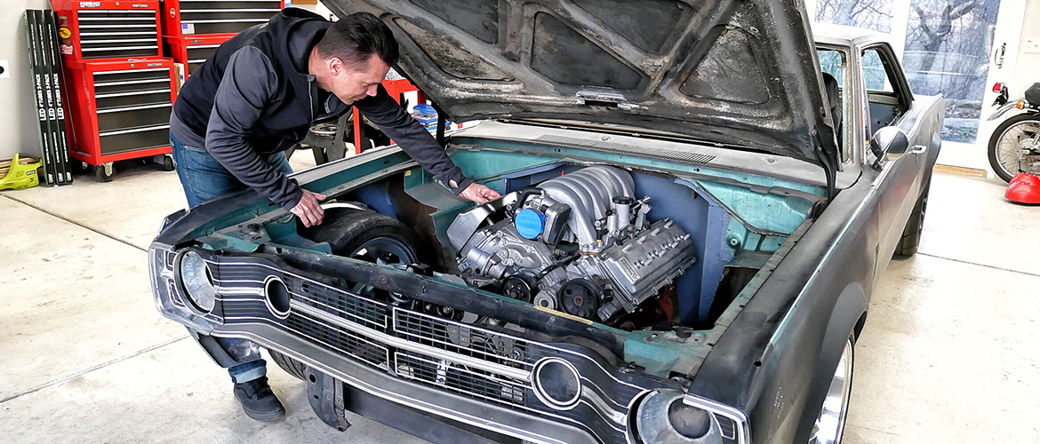 Old blue dodge challenger with a man checking out the engine