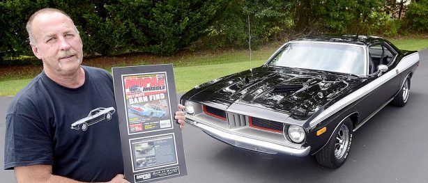 Man posing in front of his black vehicle holding up a feature story of his car in Mopar Muscle Magazine