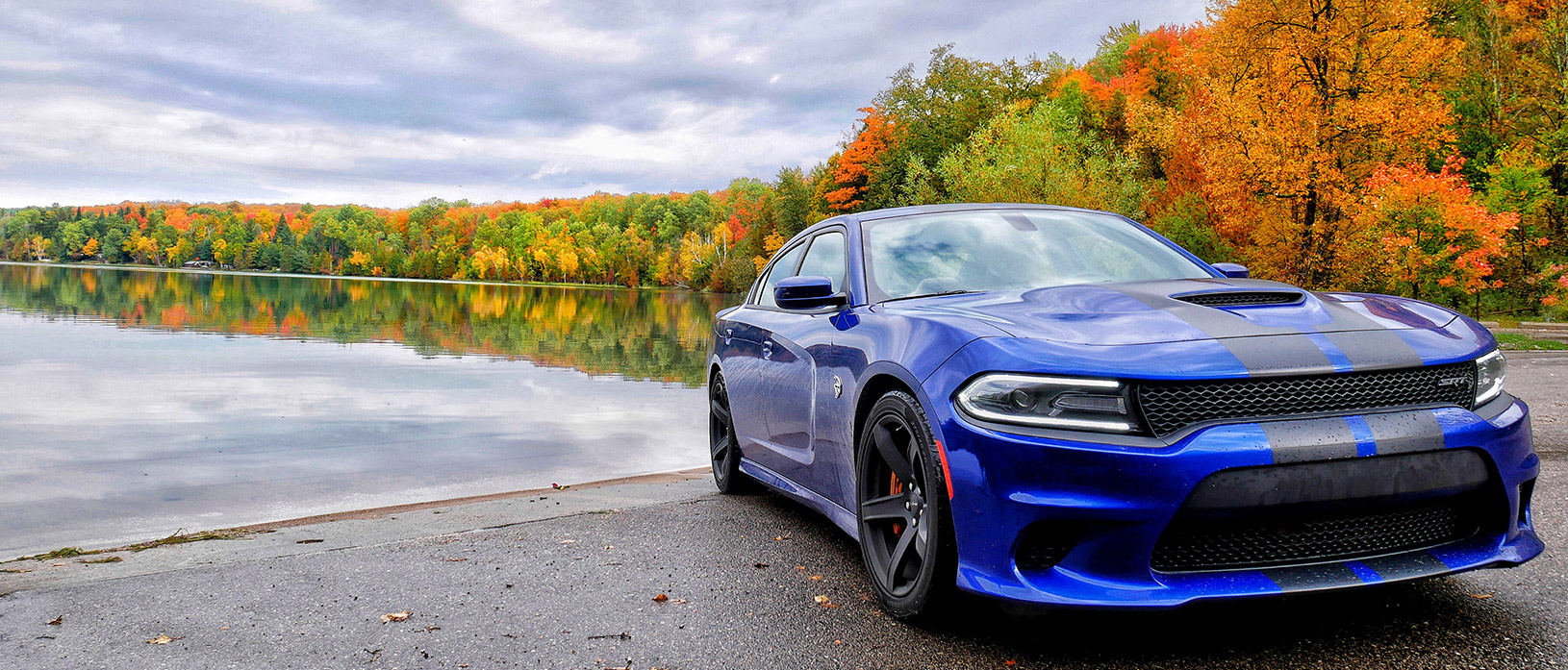 Blue 2018 Dodge Charger SRT Hellcat parked along a lake with color changing trees in background