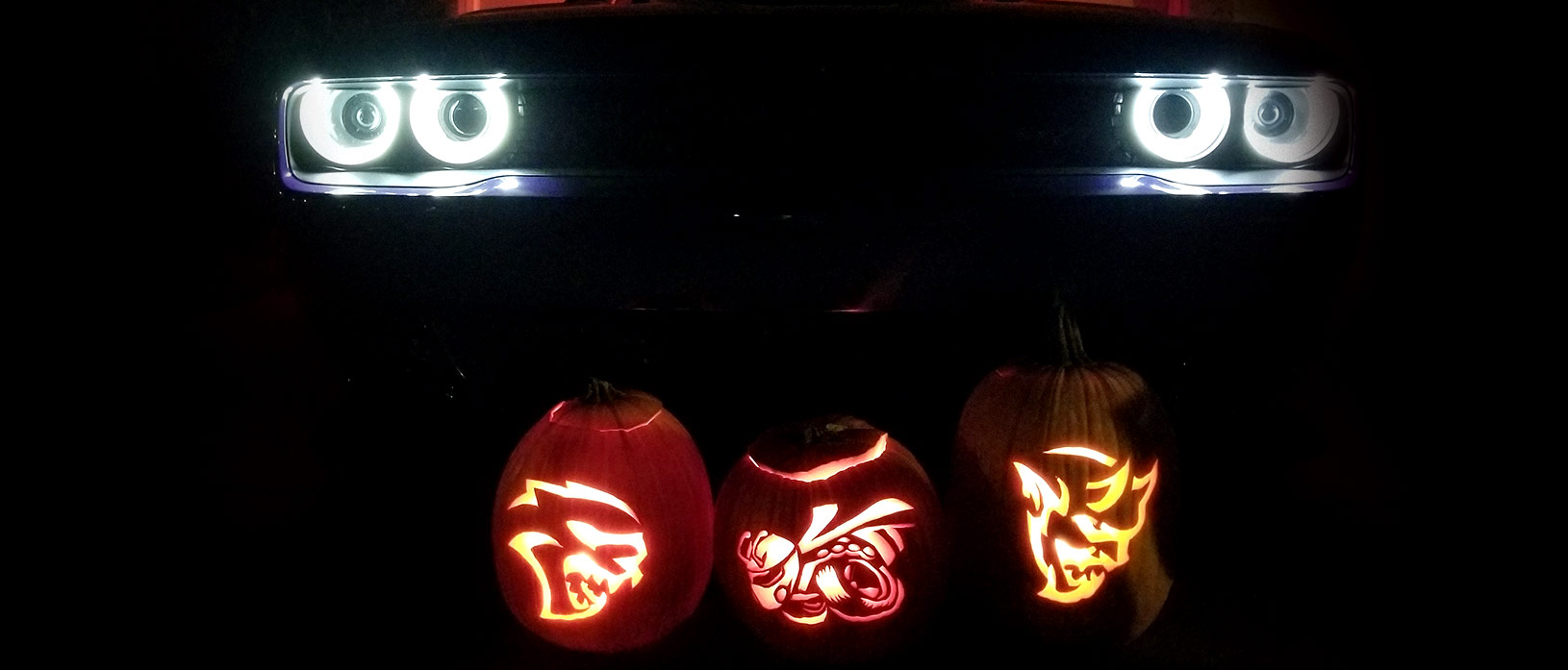 Hellcat, Angry Bee and Demon pumpkins in front of Dodge Hellcat with headlights lit.