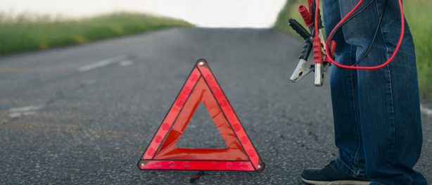 Man standing beside caution flag with jumper cables in his hand