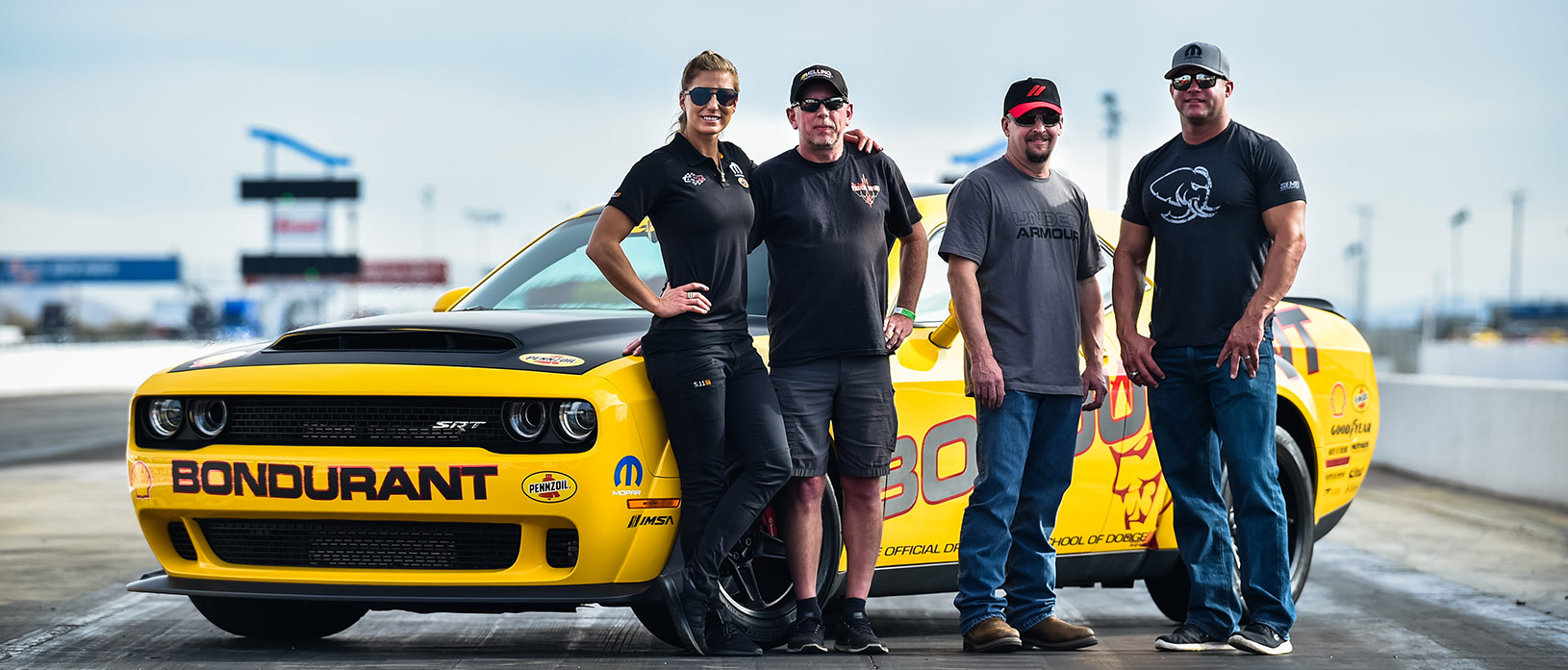 Drag Strip Showdown winners posing with Matt Hagan & Leah Pritchett in front of a yellow Bondurant Challenger