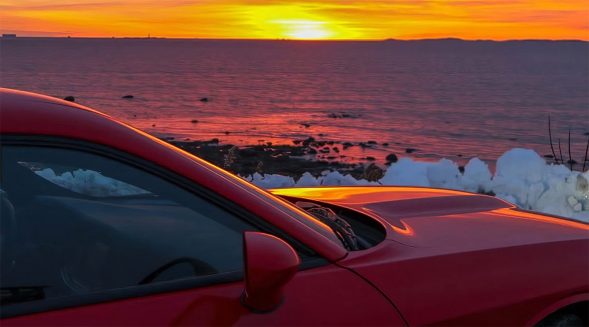 Hood of red Dodge Challenger AWD with lake and sunset in the background