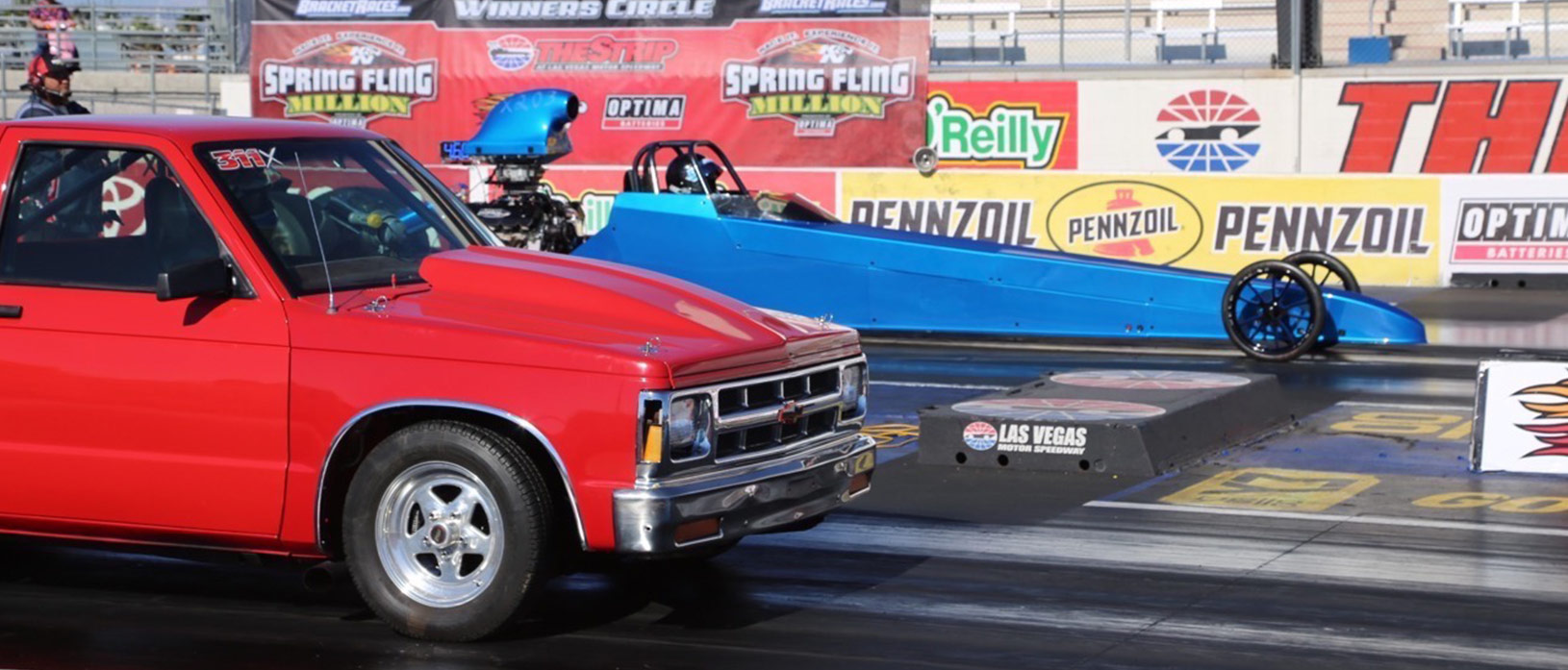 Blue dragster lining up to race a red pickup truck