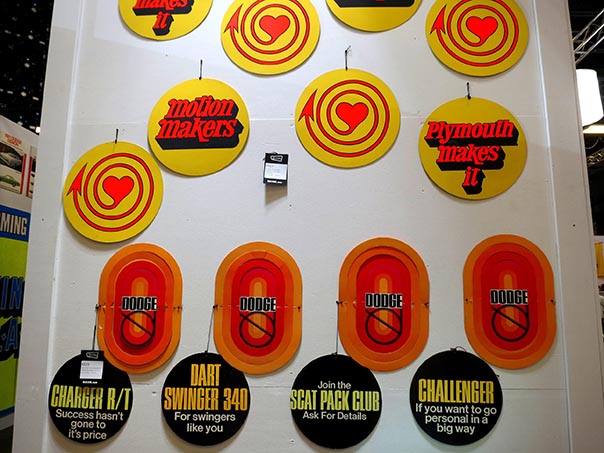 Wall of different signs, they read motin makers, Plymouth makes it, and Dodge in yellow, orange and red. Bottom row of signs are about the Charger R/T, Dart Swinger 340, Scat Pack Club, and Challenger.