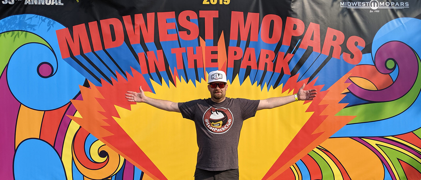 Bud Kleppe standing in front of Mopars in the Park sign