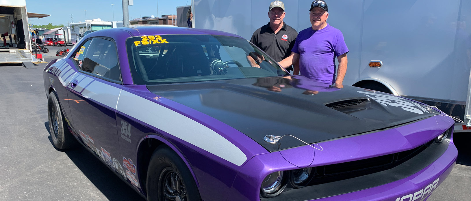 Two men posing next to purple challenger.