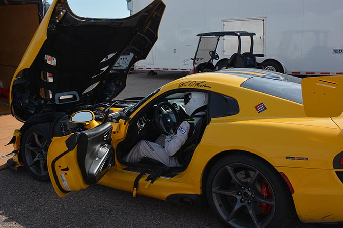 a driver wearing an all white race suit and helmet sitting in a yellow dodge viper