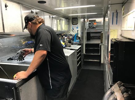 a crew member working with tools and vehicle parts inside ron capps' trailer