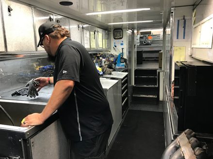 a crew member working with tools and vehicle parts inside ron capps' trailer