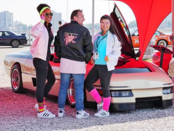 two women and one man posing with a vehicle