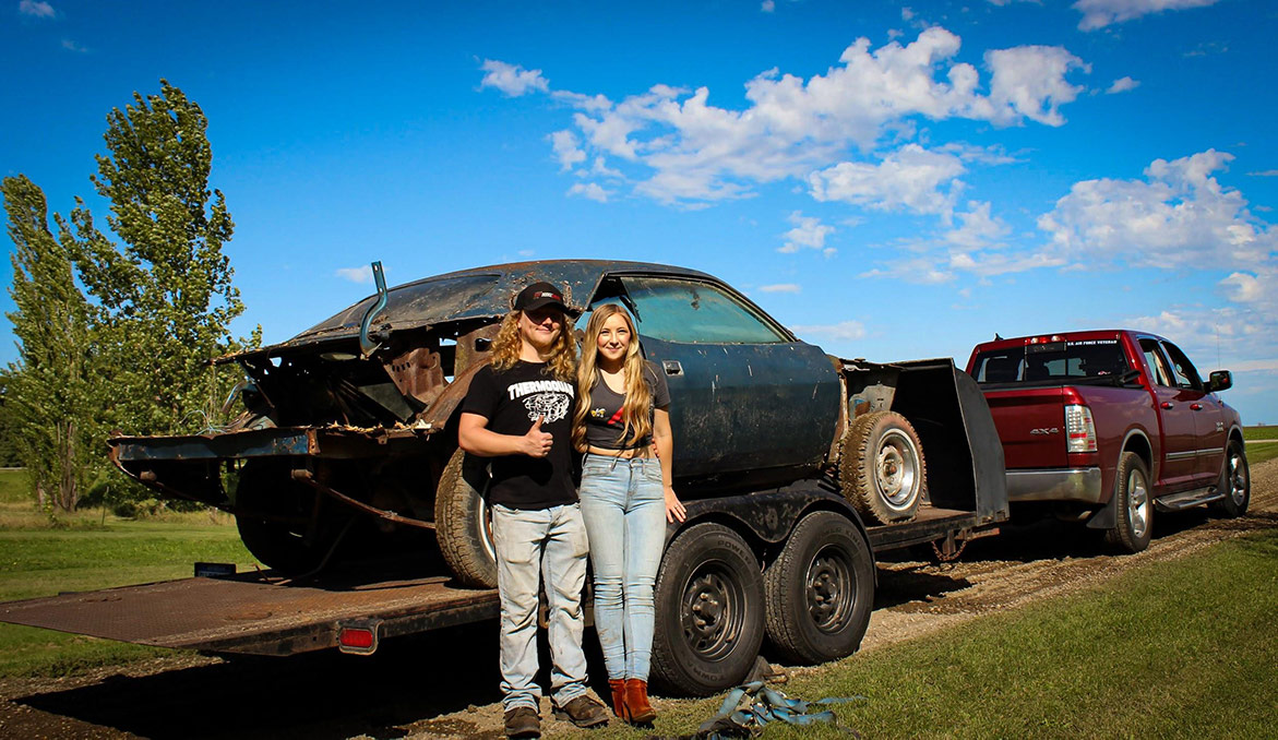 olivia crosby and her husband standing with the decrepit plymouth vehicle on a trailer bed