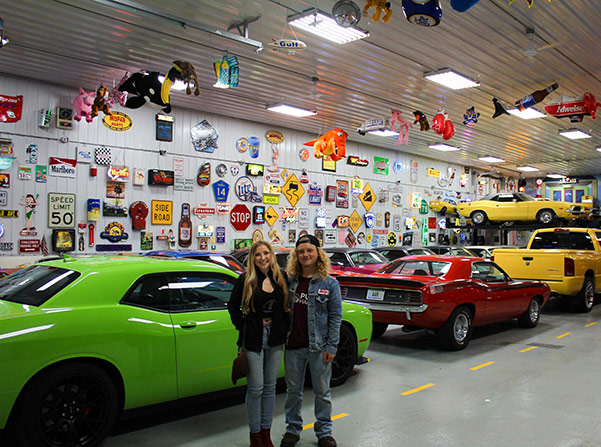 olivia crosby and luke crosby in a garage with several vehicles