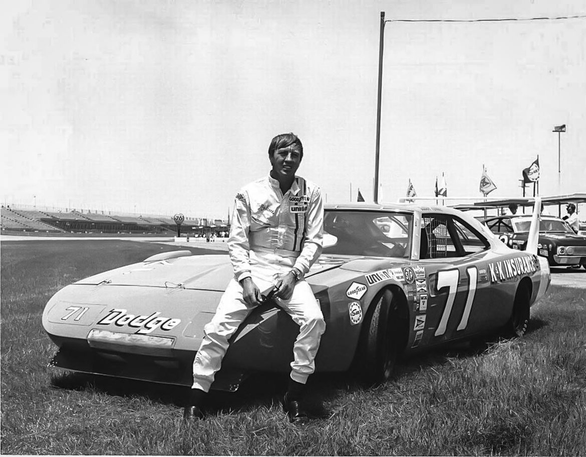 man sitting on the hood of a dodge racing vehicle