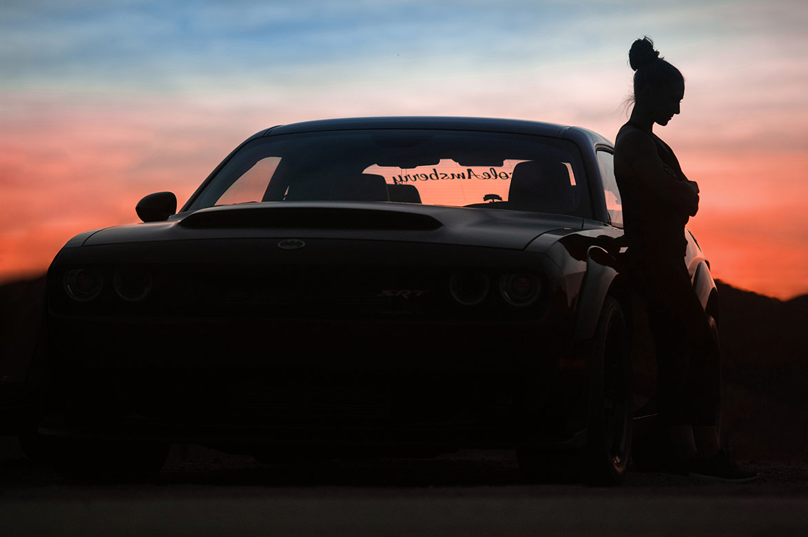 Woman next to a dodge challenger at sunset