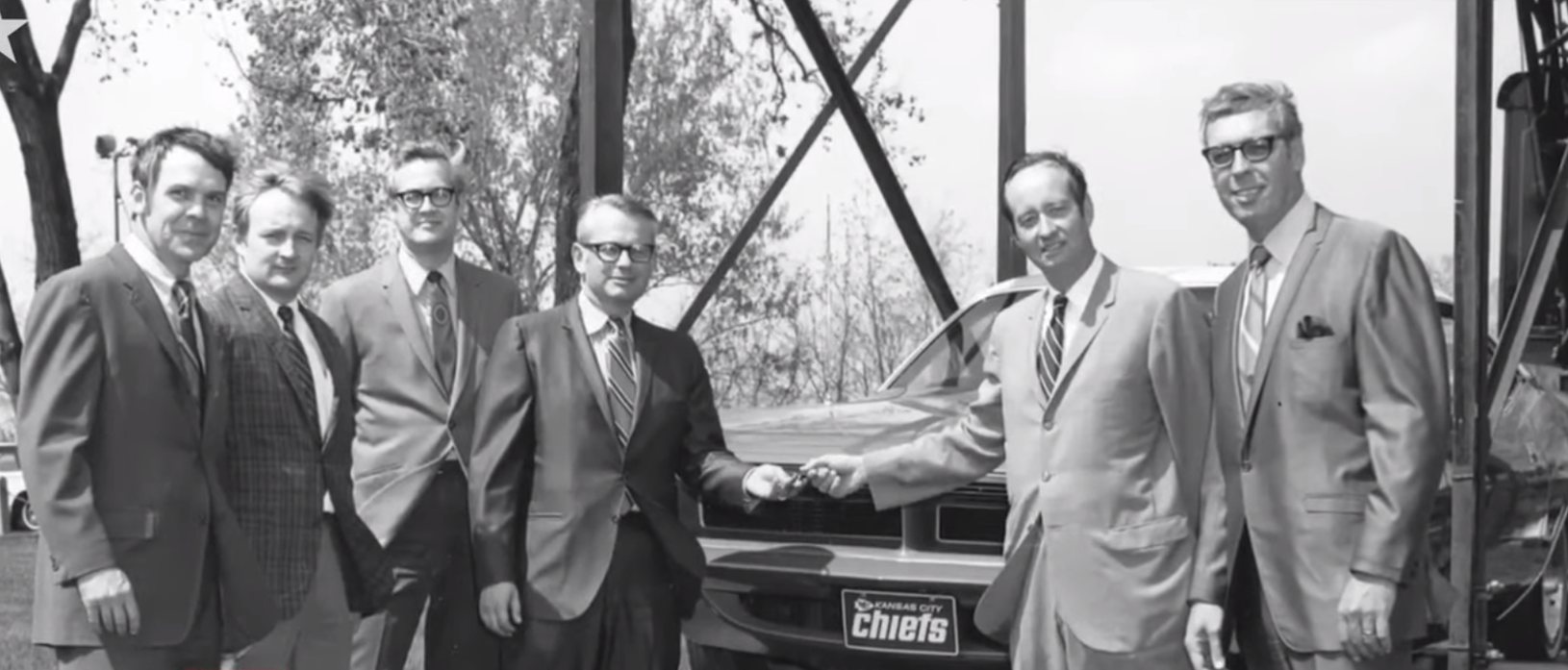 Men standing around a 1970 plymouth cuda