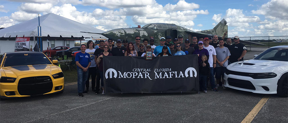 club members group picture with cars and a banner