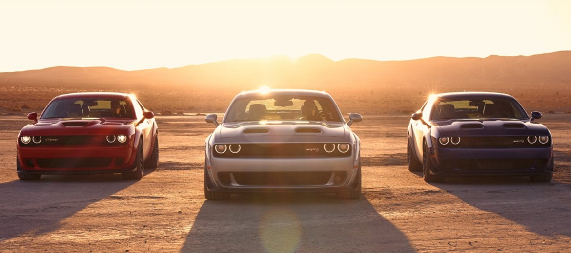Three Dodge Challengers parked in front of a sunset