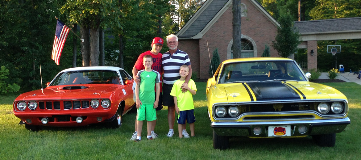 Family posing in front of classic Mopar vehicles