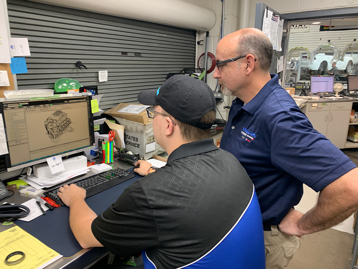 Two men looking at a vehicle engine on a computer