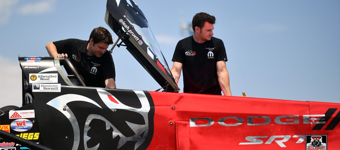 Two crew members taking a top fuel dragster out of the trailer