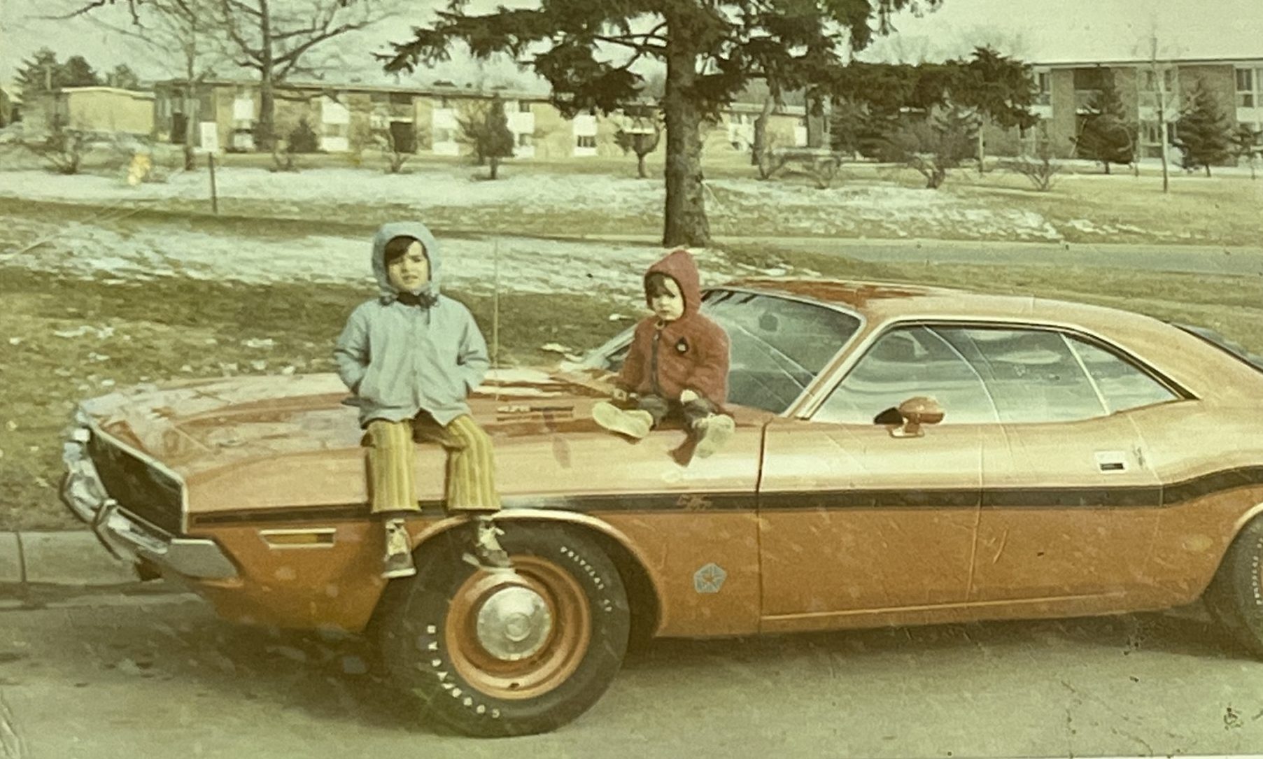 2 kids sitting on the hood of a Dodge vehicle
