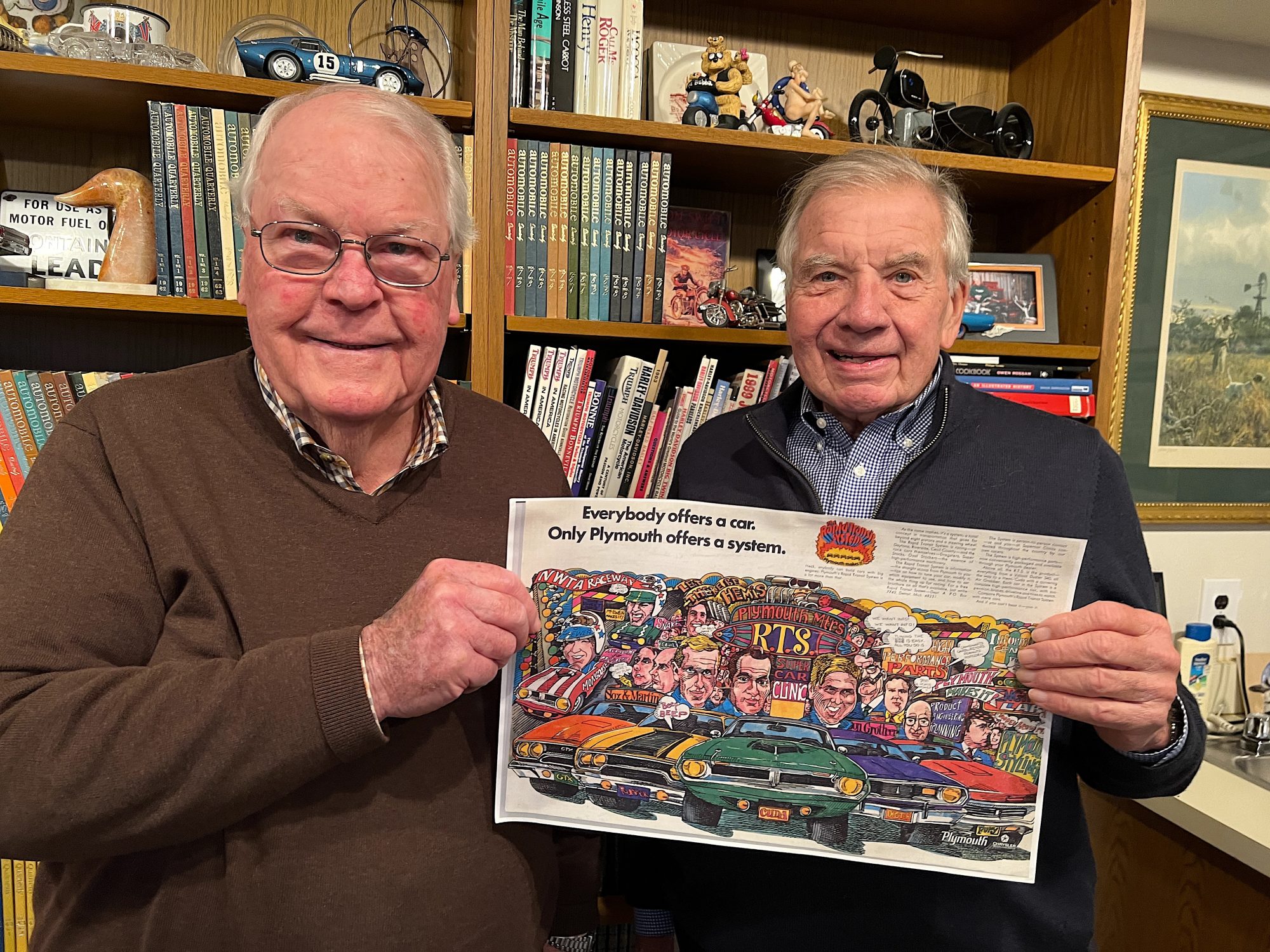 Two men holding up a vintage Plymouth ad