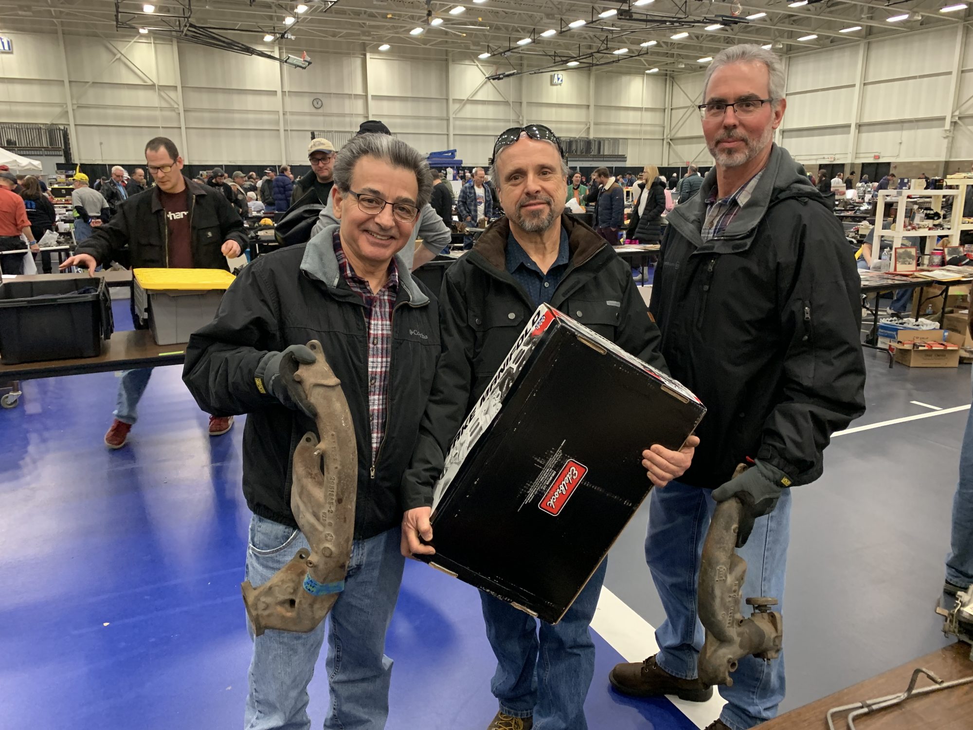 three men holding up their finds at a swap meet