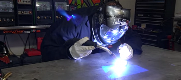 A welder using a MIG tool in his shop