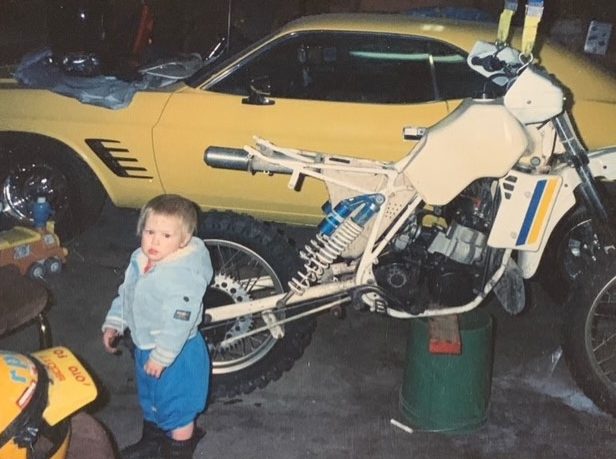 Little boy standing next to a Challenger and a motorcycle