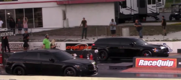 Two black Dodge Magnum vehicles on the starting line of a drag strip
