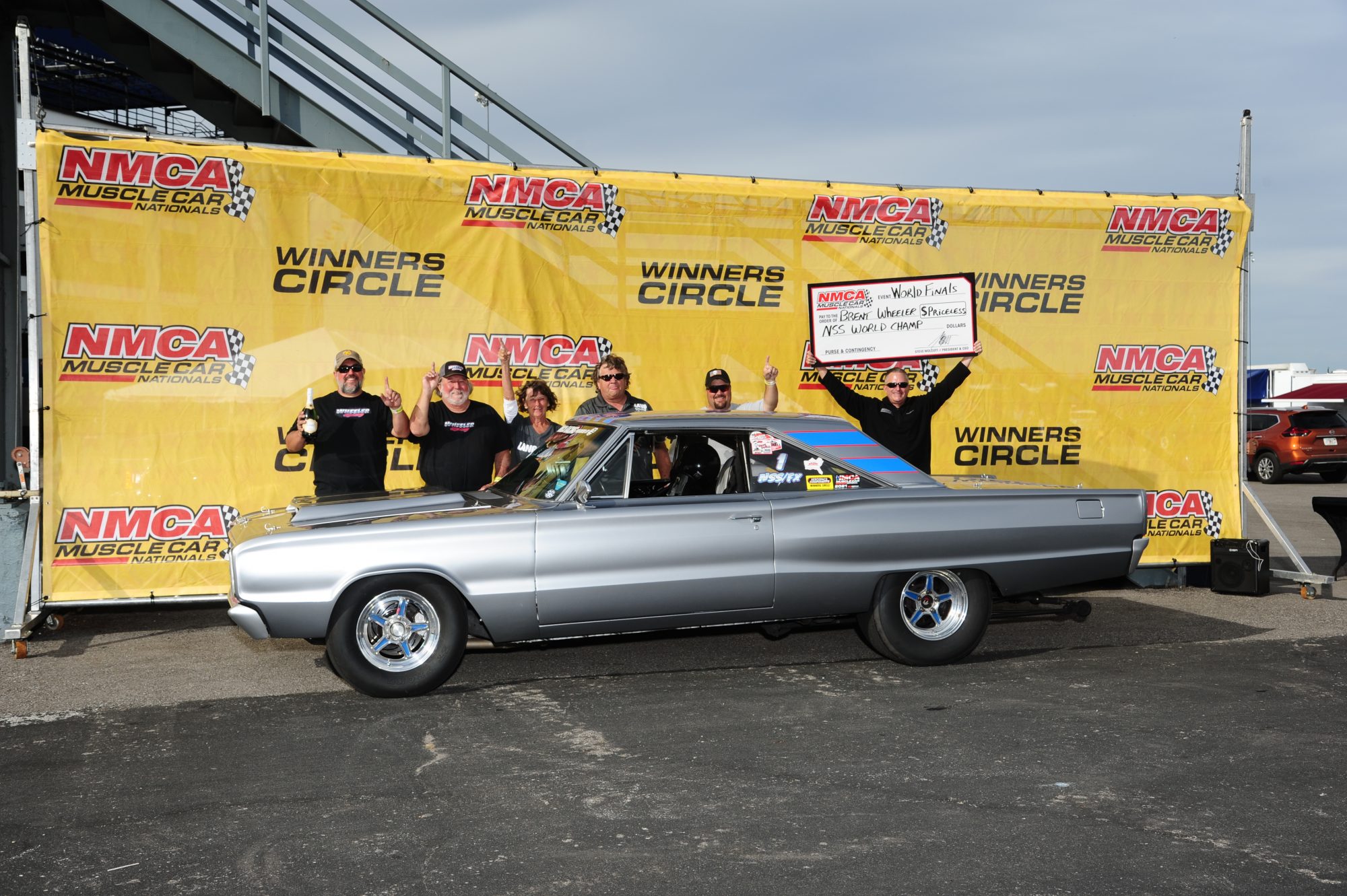 man holding up check next to his car in the winners circle