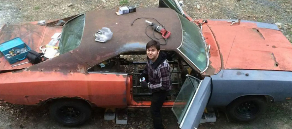 Young man next to a gutted, rusted '69 Charger